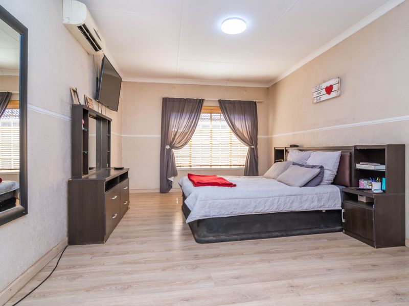 A bedroom featuring laminate flooring, a split-system air conditioner, and window blinds, offering a functional space with neutral wall finishes.