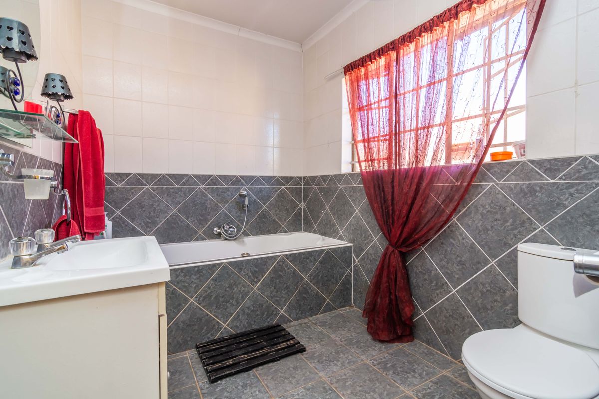 A functional bathroom featuring a built-in bathtub, vanity basin, and toilet with neutral wall and floor tiling.