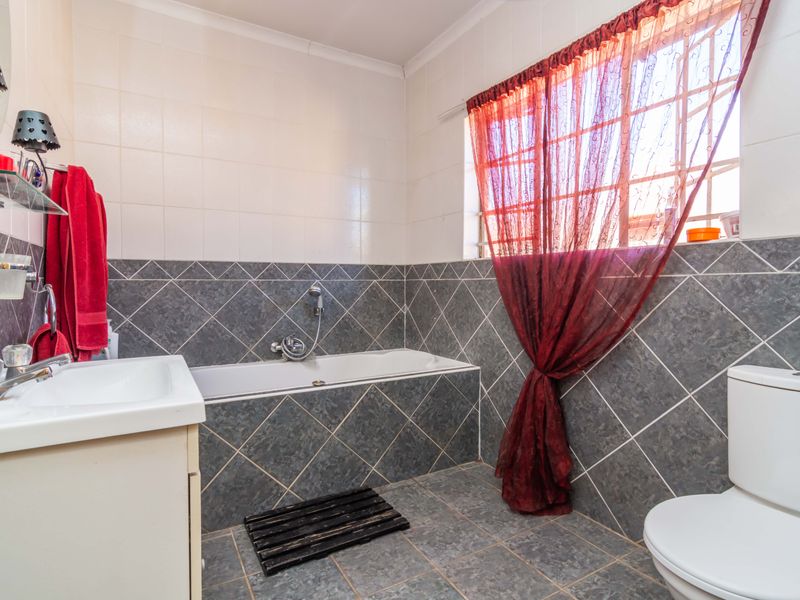 A functional bathroom featuring a built-in bathtub, vanity basin, and toilet with neutral wall and floor tiling.