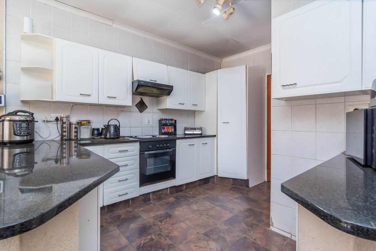 A functional kitchen featuring white built-in cabinetry, dark granite countertops, a built-in oven with hob, and tiled splashbacks.