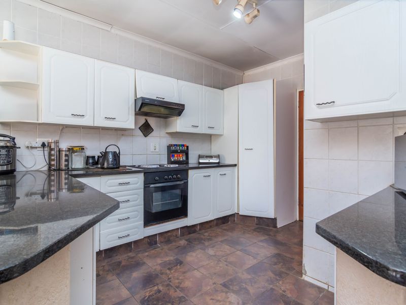 A functional kitchen featuring white built-in cabinetry, dark granite countertops, a built-in oven with hob, and tiled splashbacks.
