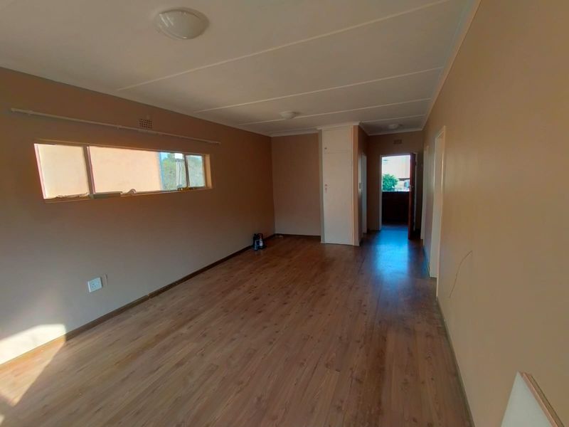 An empty living room featuring laminate flooring, a built-in cupboard, and neutral wall tones, offering a blank canvas for interior design.
