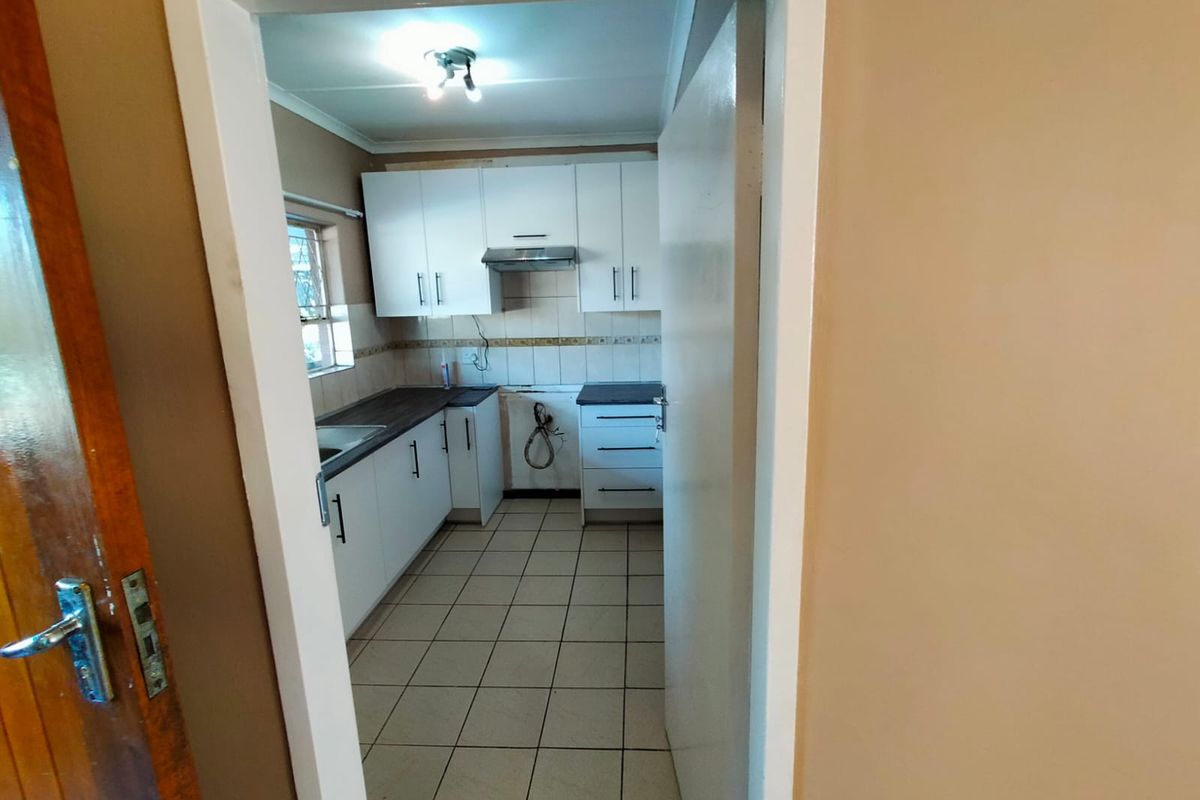 A functional kitchen featuring white cabinetry, dark countertops, tiled flooring, and a built-in extractor fan, viewed through a doorway.