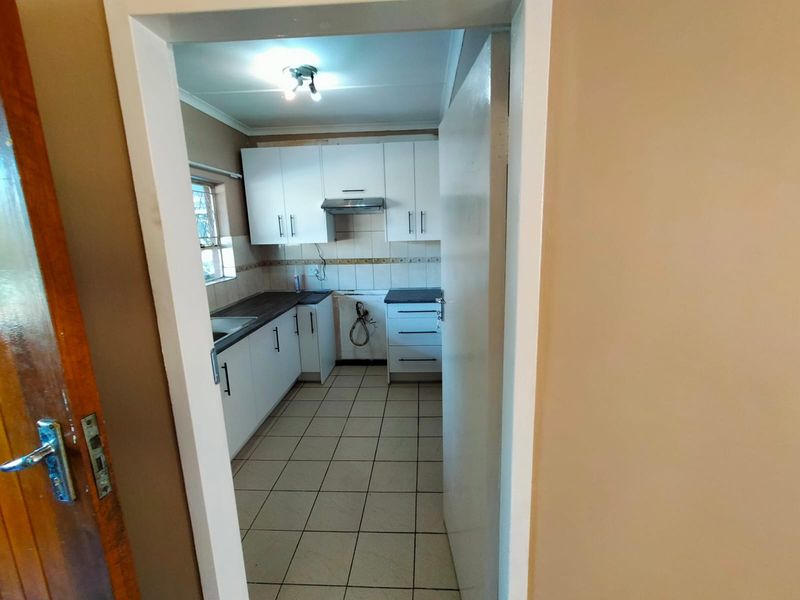 A functional kitchen featuring white cabinetry, dark countertops, tiled flooring, and a built-in extractor fan, viewed through a doorway.