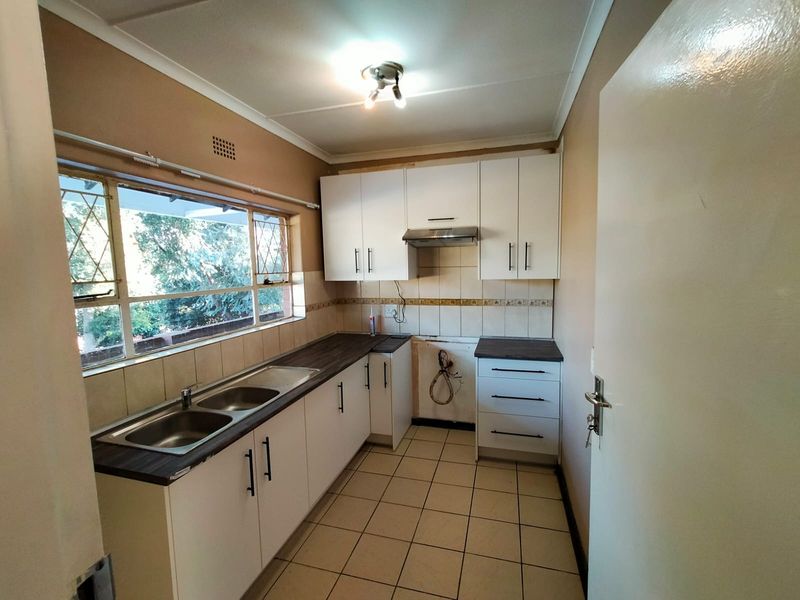 A functional kitchen featuring white cabinetry, laminate countertops, a double stainless steel sink, and tiled flooring, currently awaiting a stove or oven installation.
