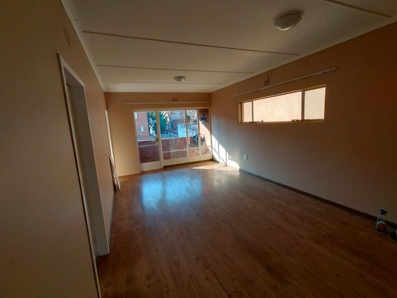 An empty living room featuring laminate flooring, a sliding glass door leading to a balcony, and natural light from a horizontal window.