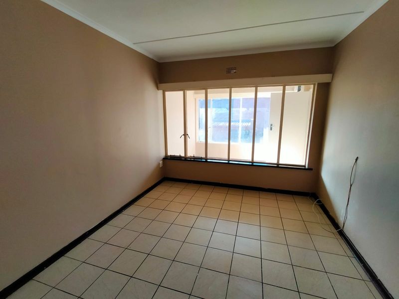 An empty bedroom featuring neutral wall paint, tiled flooring, and a large window providing natural light.