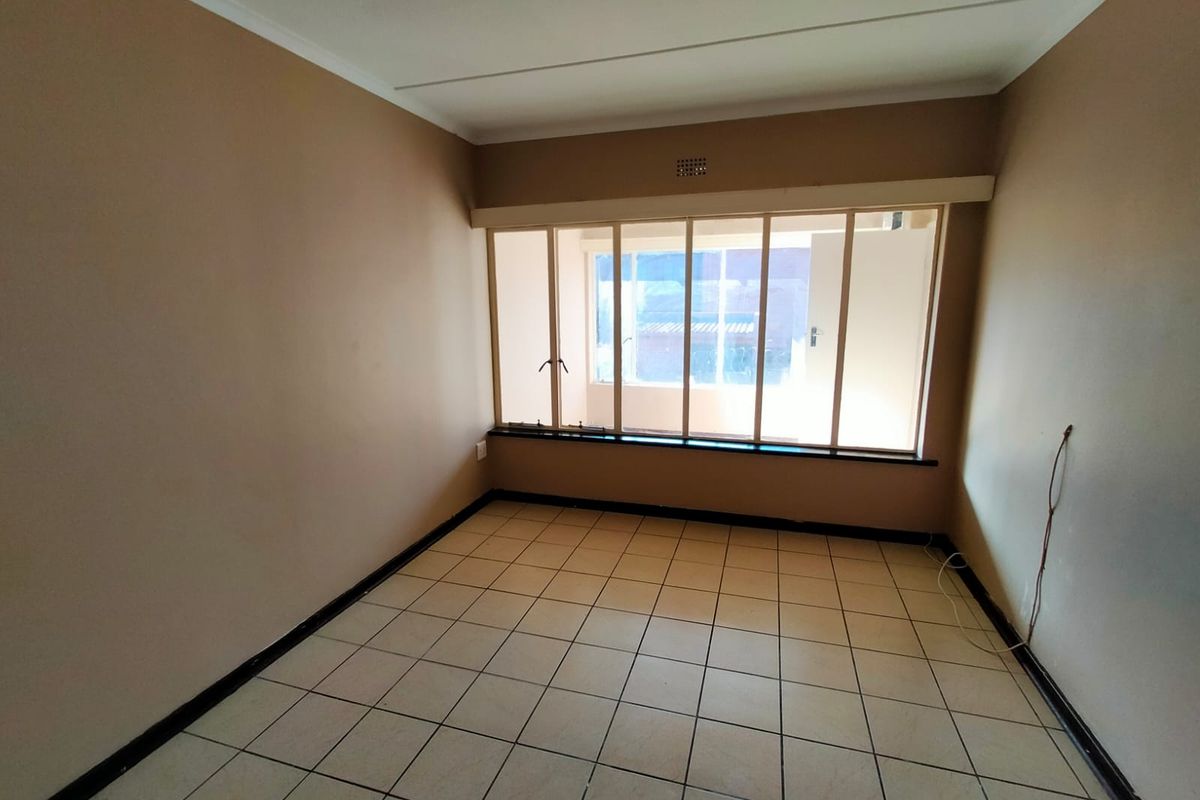 An empty bedroom featuring tiled flooring, a large multi-pane window, and neutral wall paint, offering a blank canvas for potential renovation or staging.