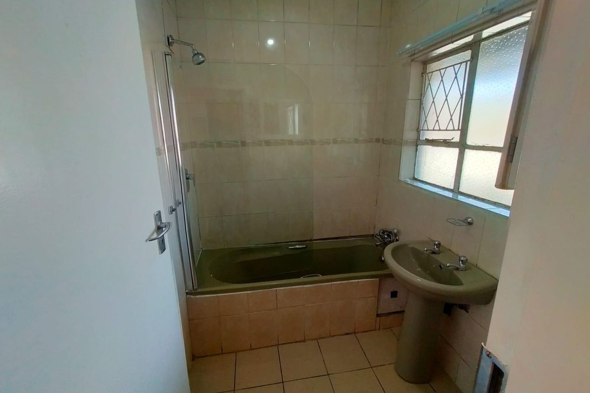A dated bathroom featuring a bathtub with shower attachment, pedestal basin, and tiled finishes, offering potential for a modern renovation.