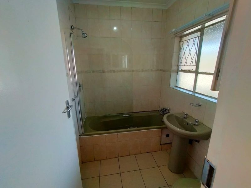 A dated bathroom featuring a bathtub with shower attachment, pedestal basin, and tiled finishes, offering potential for a modern renovation.