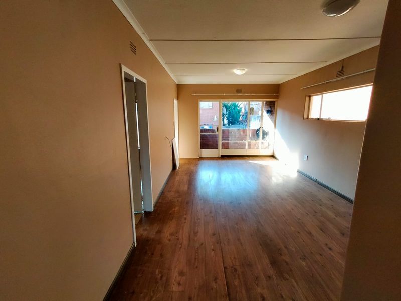 An empty, open-plan living area featuring laminate wood flooring, neutral wall tones, and a sliding glass door providing access to an outdoor space.