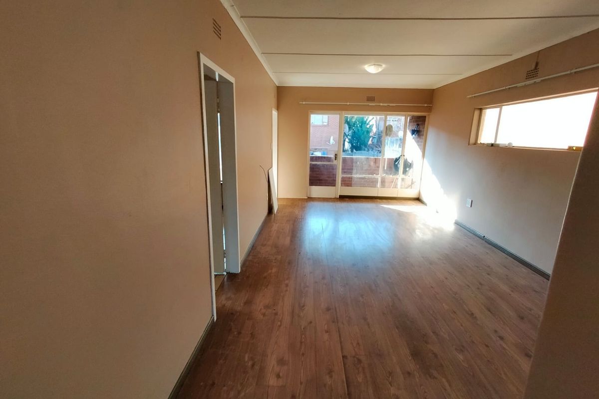 An empty, open-plan living area featuring laminate flooring, neutral wall tones, and a sliding glass door leading to an outdoor balcony space.