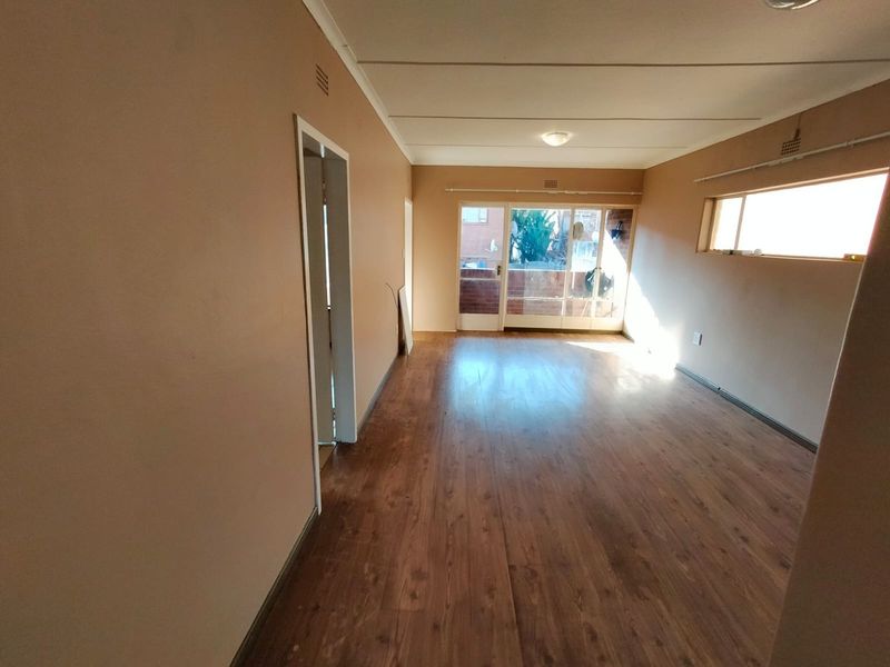 An empty, open-plan living area featuring laminate flooring, neutral wall tones, and a sliding glass door leading to an outdoor balcony space.