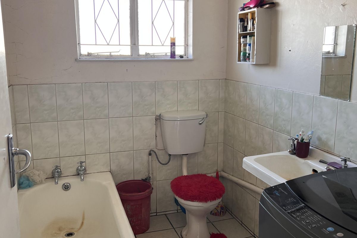 A functional bathroom featuring a bathtub, toilet, and washbasin with tiled finishes, requiring cosmetic updates and maintenance to improve its overall condition.