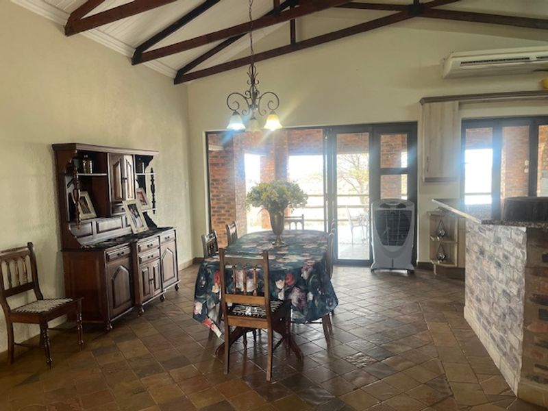 Open-plan living and dining area featuring vaulted ceilings with exposed timber beams, stone tile flooring, and a brick-clad breakfast bar with granite countertops.