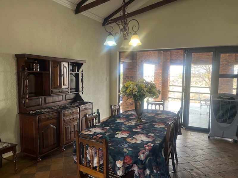 Dining room featuring exposed timber ceiling beams, terracotta floor tiles, and large sliding glass doors providing access to the outdoor patio area.