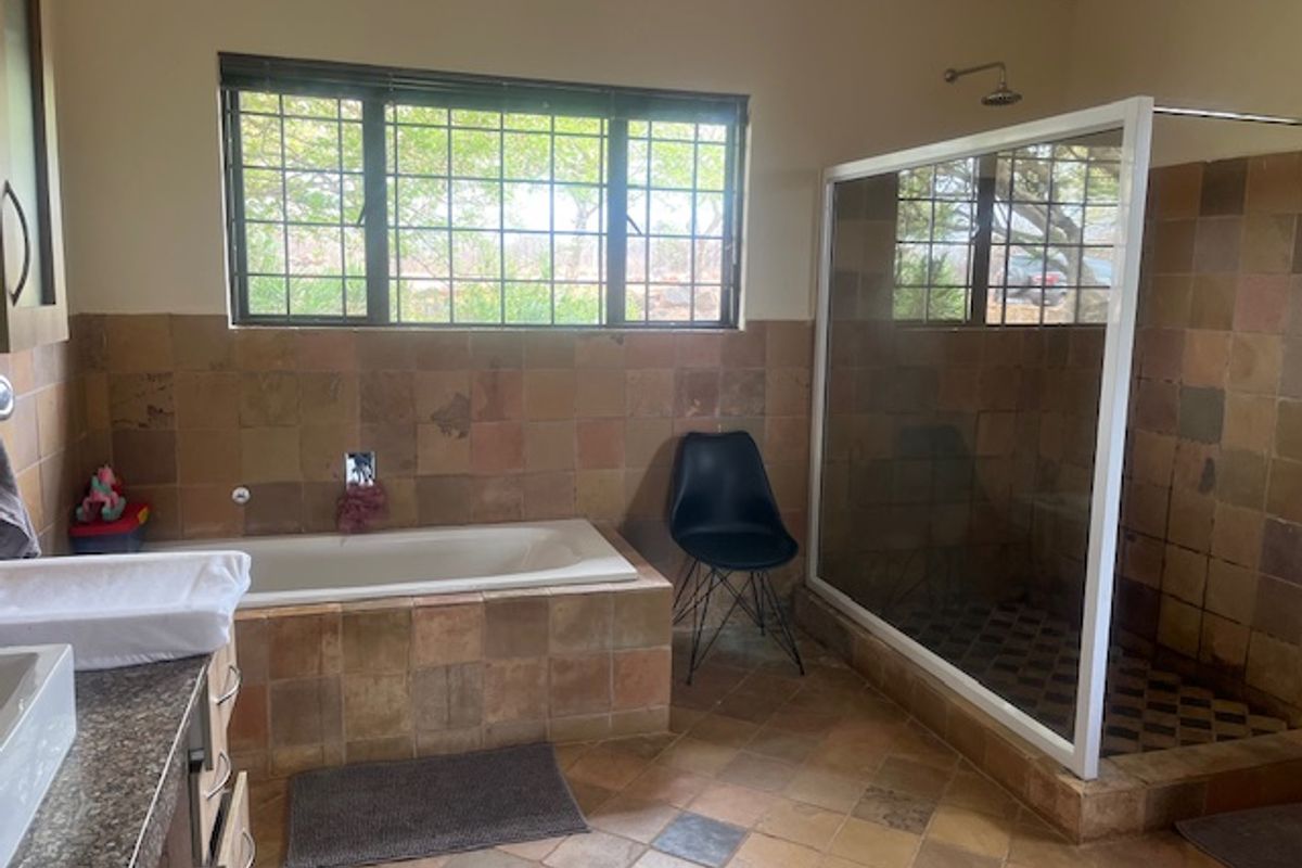 A spacious bathroom featuring a built-in bathtub, a separate walk-in shower, and tiled finishes throughout, offering a functional layout with natural light.