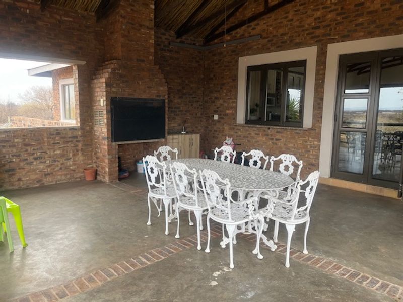 Spacious covered patio featuring exposed brick walls, a built-in braai, and a rustic thatched roof, offering an ideal space for outdoor entertaining.