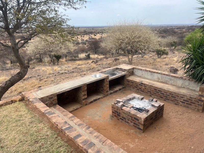 Outdoor entertainment area featuring a built-in brick braai, concrete prep surface with sink, and a central brick fire pit overlooking the natural landscape.