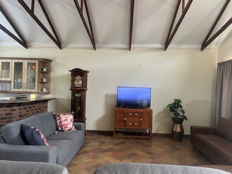 Spacious open-plan living area featuring a high vaulted ceiling with exposed timber beams, terracotta tile flooring, and a brick-accented kitchen breakfast bar.