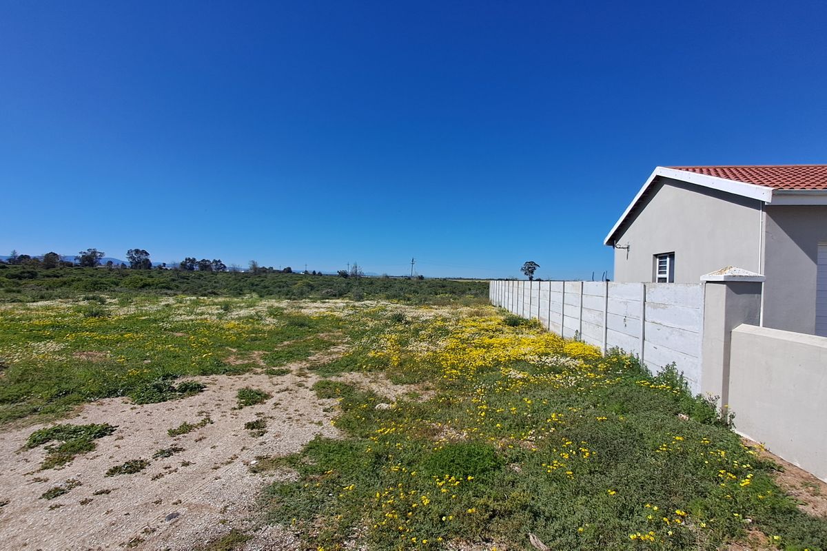 A view of the rear section of the residential property, featuring a large open plot of land adjacent to a modern home with boundary walling.