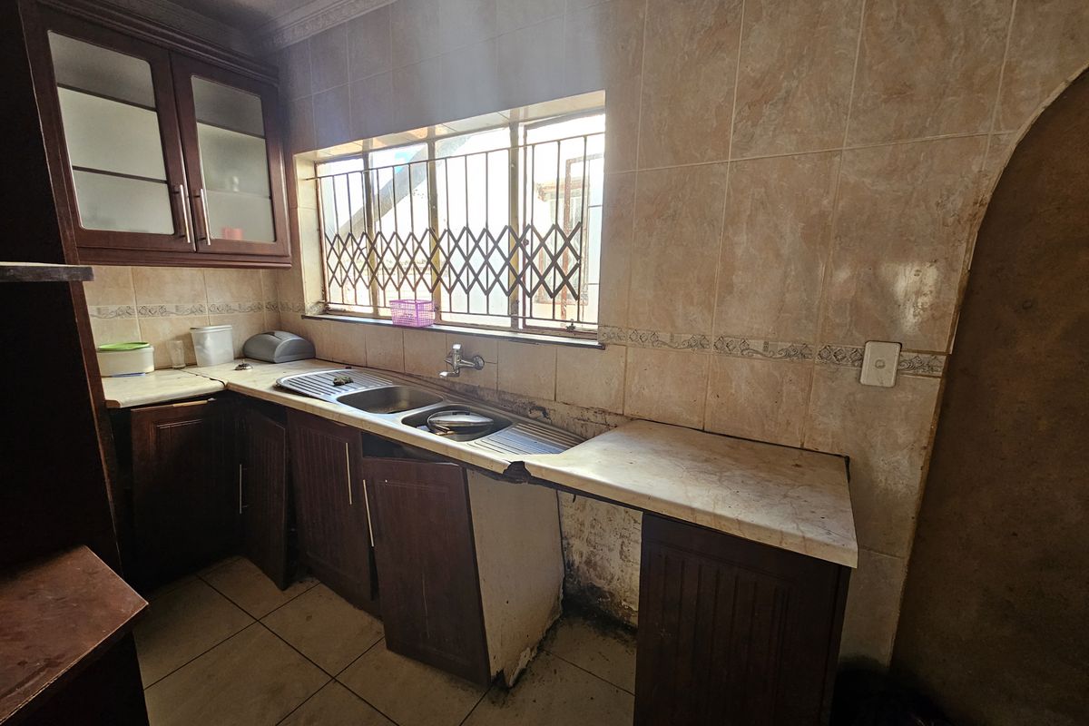 A dated kitchen featuring dark wood cabinetry, tiled walls, and a double sink, requiring significant maintenance and cosmetic updates to improve functionality and aesthetic appeal.