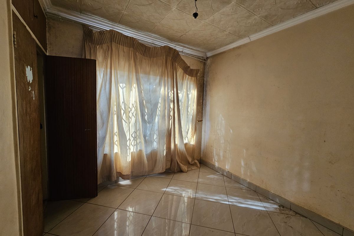 An empty bedroom featuring tiled flooring, built-in cupboards, and textured ceiling tiles, requiring cosmetic updates and repairs to the walls and ceiling.