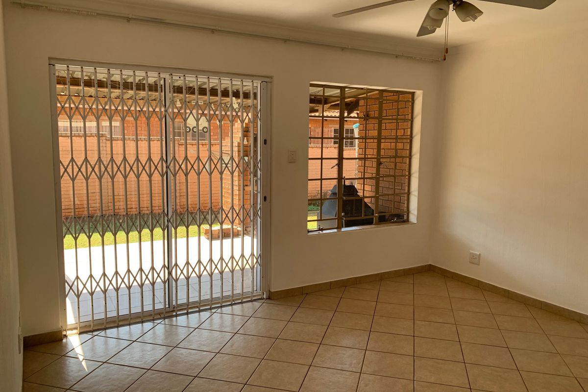 An empty living room featuring tiled flooring, a ceiling fan, and a sliding glass door with a security gate leading to the rear patio.