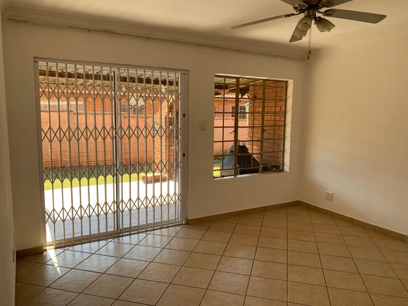 An empty living room featuring tiled flooring, a ceiling fan, and a sliding glass door with a security gate leading to the rear patio.
