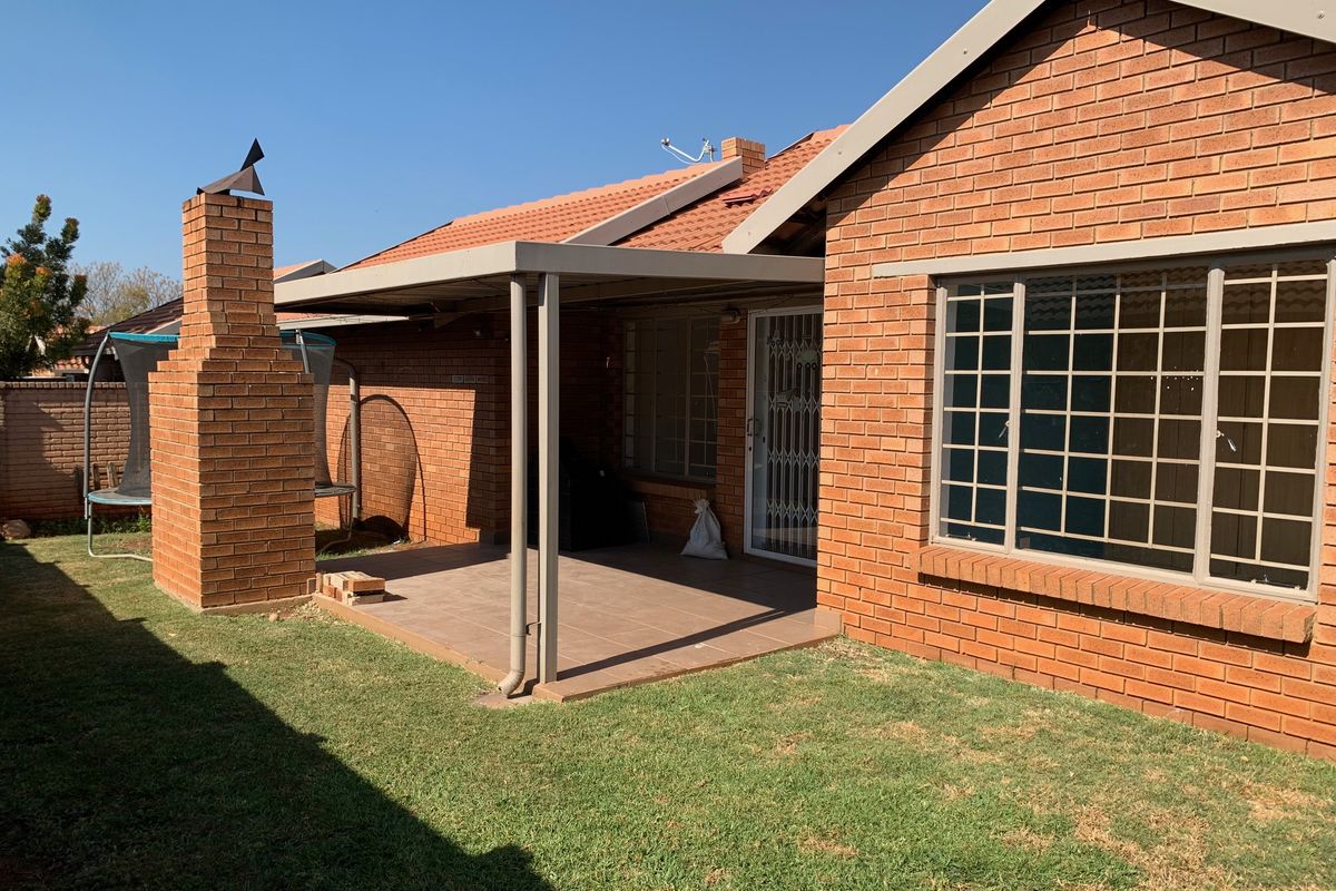 Rear view of the townhouse featuring a covered patio with a built-in brick chimney, tiled flooring, and secure window bars.