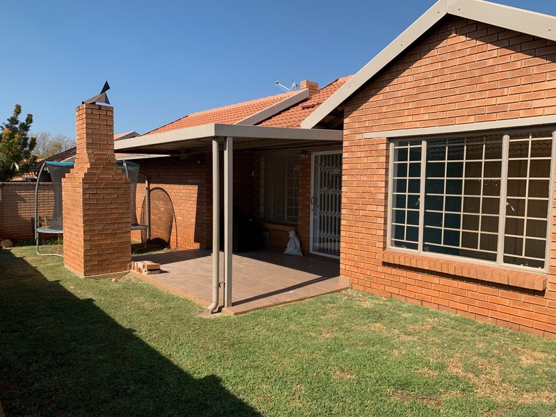 Rear view of the townhouse featuring a covered patio with a built-in brick chimney, tiled flooring, and secure window bars.