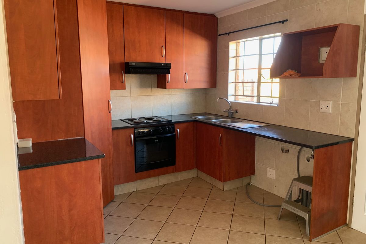 A functional kitchen featuring wood-look cabinetry, granite countertops, built-in oven, hob, and tiled finishes, offering a practical layout for daily use.