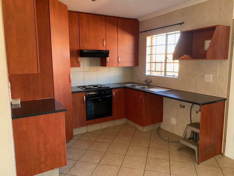 A functional kitchen featuring wood-look cabinetry, granite countertops, built-in oven, hob, and tiled finishes, offering a practical layout for daily use.