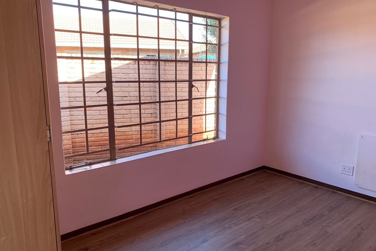 An empty bedroom featuring laminate flooring, a built-in wardrobe, and a window fitted with security bars.