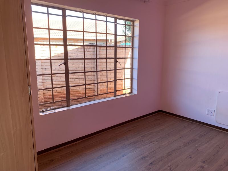 An empty bedroom featuring laminate flooring, a built-in wardrobe, and a window fitted with security bars.
