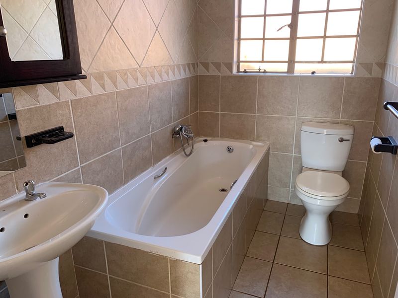 A functional bathroom featuring a pedestal basin, built-in bathtub, and toilet, finished with neutral wall and floor tiling.