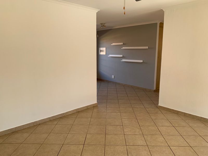 An empty living area featuring neutral wall tones, ceramic floor tiles, and built-in wall shelving, offering a versatile space ready for personalization.
