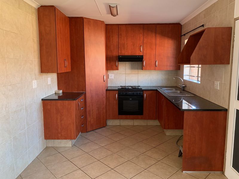 A functional kitchen featuring wooden cabinetry, granite countertops, built-in oven and hob, and tiled finishes throughout.