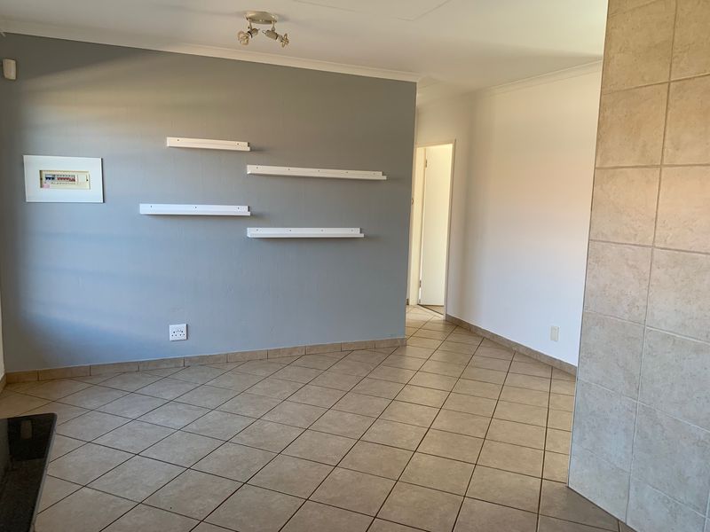 An empty living area featuring neutral ceramic floor tiles, a grey accent wall with built-in shelving, and a tiled feature pillar.