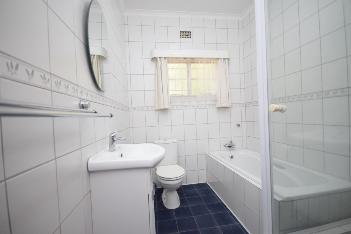 A functional bathroom featuring a vanity basin, toilet, and a combined bathtub and shower enclosure with classic white wall tiling.