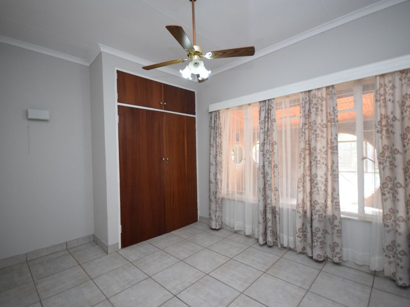 A bright, empty bedroom featuring tiled flooring, built-in wooden cupboards, and a ceiling fan, offering a clean canvas for personalization.