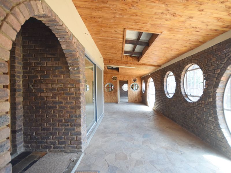 A spacious covered patio featuring unique circular windows, exposed brick walls, a timber-clad ceiling, and durable stone flooring.