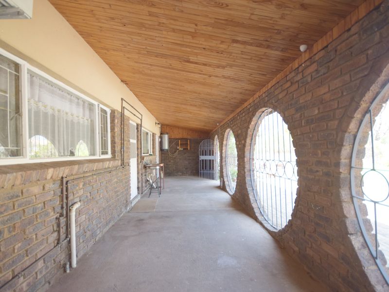 A covered outdoor patio featuring distinctive circular brick openings, a timber-clad ceiling, and concrete flooring, providing a sheltered transition space.
