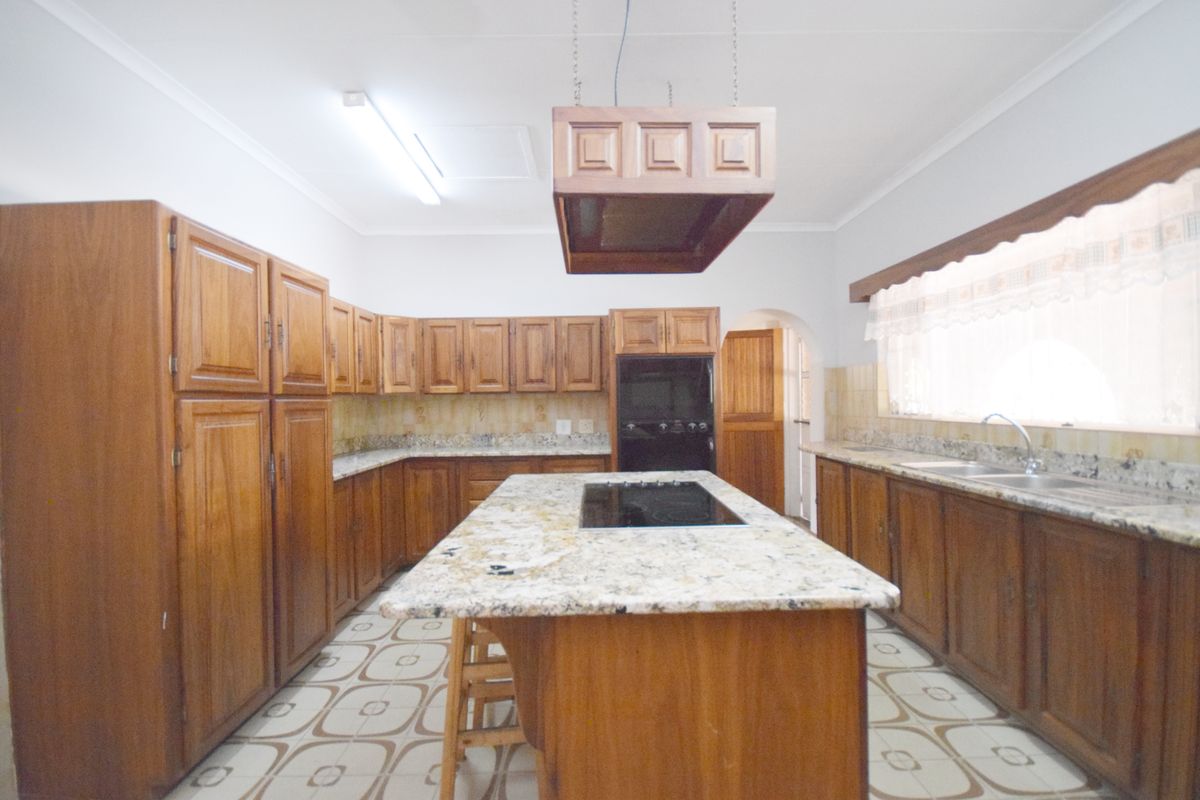 Spacious kitchen featuring extensive wooden cabinetry, granite countertops, a central island with a built-in hob, and a double sink setup.