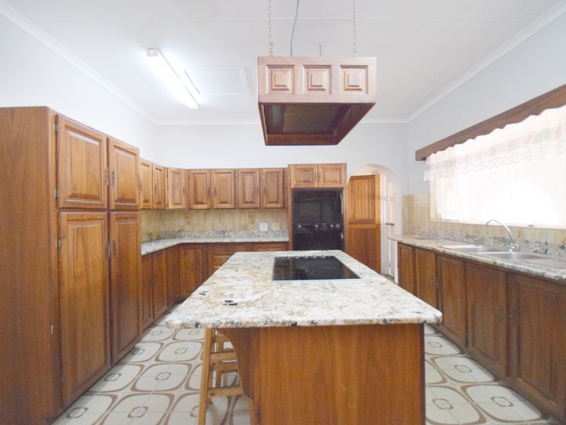Spacious kitchen featuring extensive wooden cabinetry, granite countertops, a central island with a built-in hob, and a double sink setup.