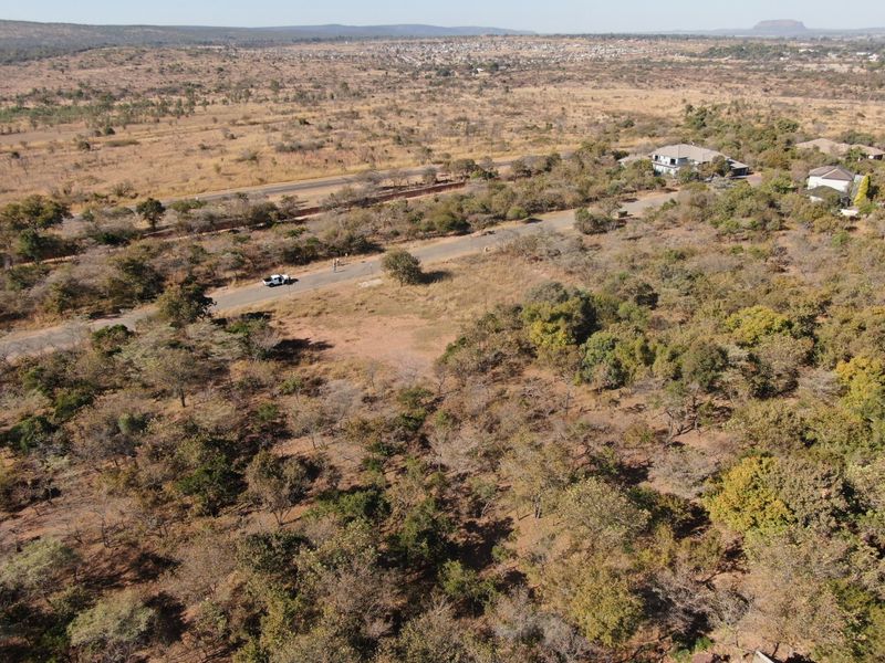 An aerial view of a large, undeveloped residential plot featuring native vegetation and direct access to a paved road in a quiet area.