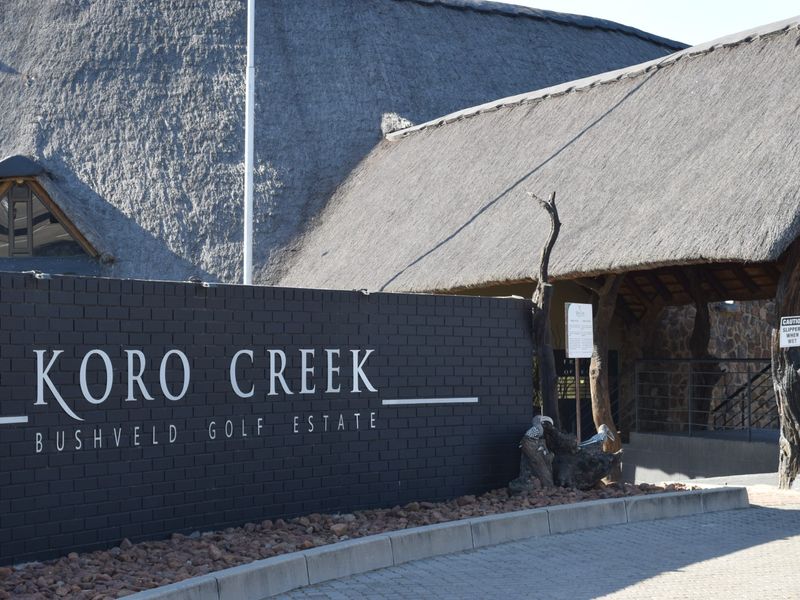 Entrance view of Koro Creek Bushveld Golf Estate featuring a prominent brick signage wall and traditional thatched roof architecture.
