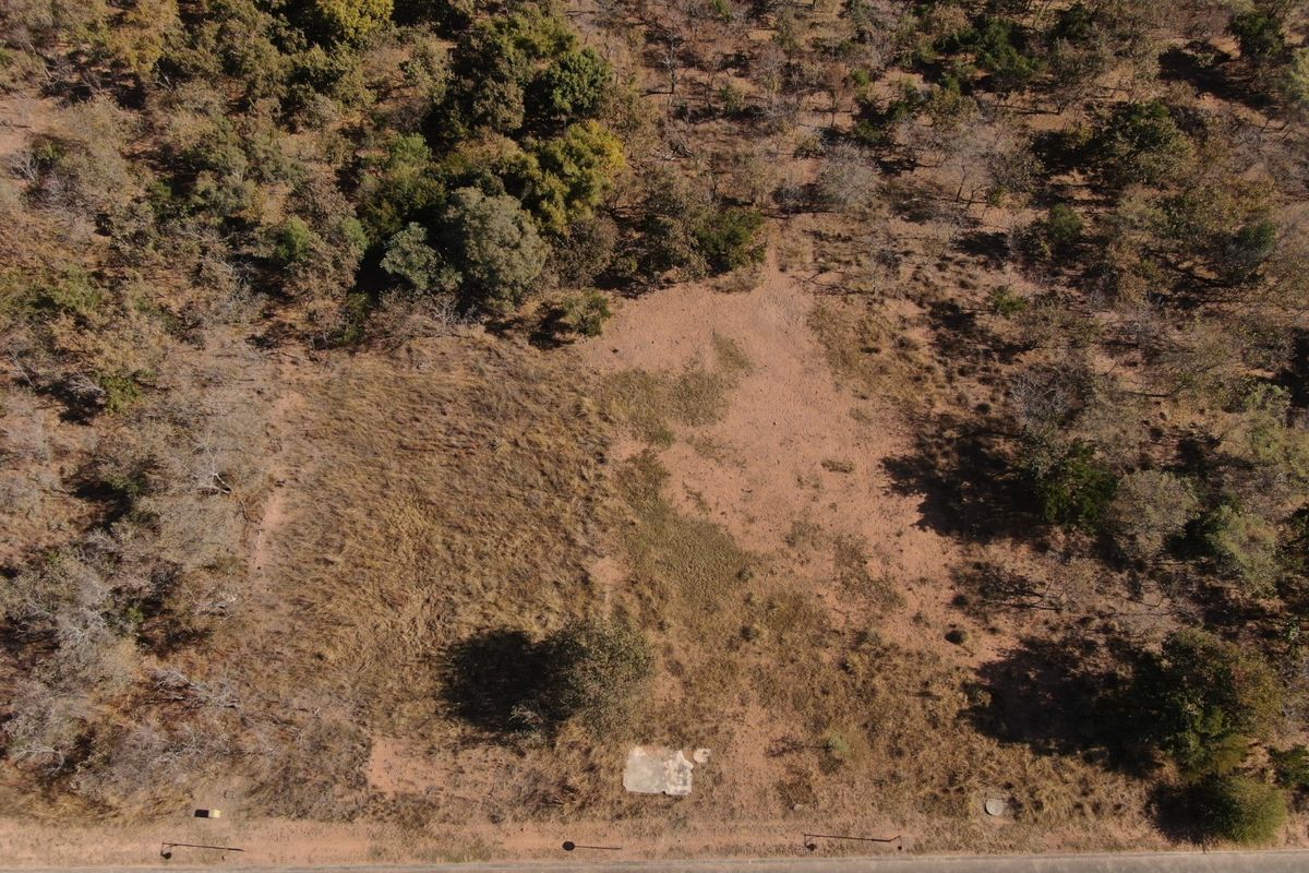 An aerial view of a vacant residential plot featuring natural vegetation and a small concrete foundation slab.