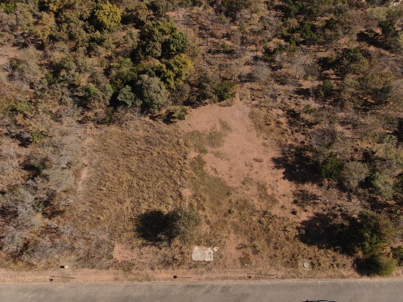 An aerial view of a vacant residential plot featuring natural vegetation and a small concrete foundation slab.