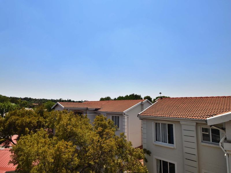 An elevated view overlooking neighbouring residential buildings with terracotta tiled roofs and mature trees under a clear blue sky.